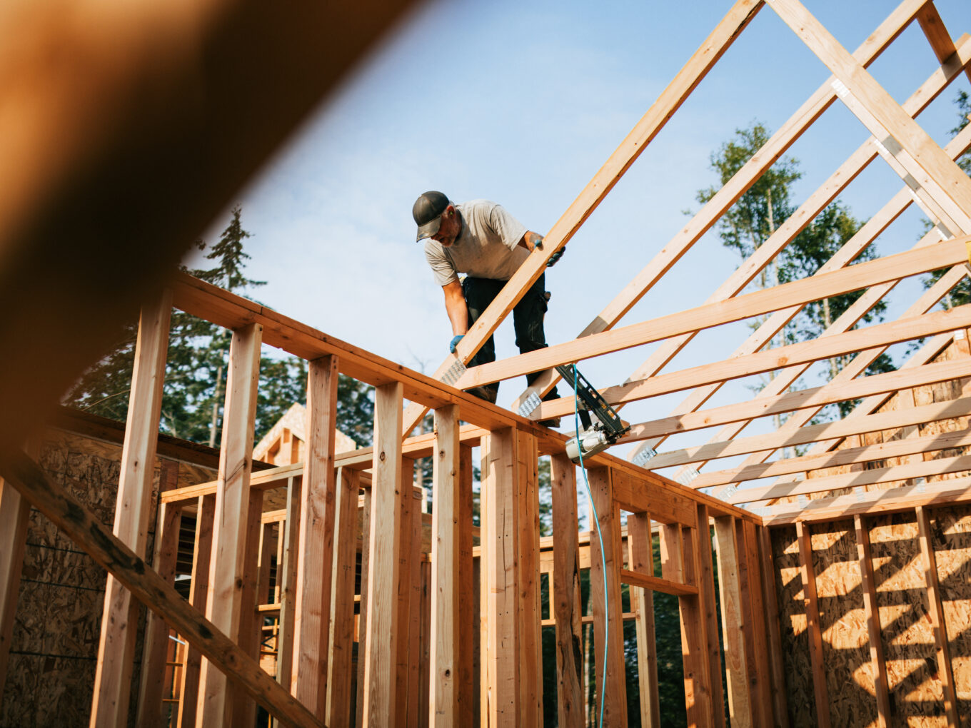 Workers build the frame of a new house project. Bare plywood and beams as it is framed up from the foundation. High lumber costs have affected the building process. Shot in Washington state, USA.