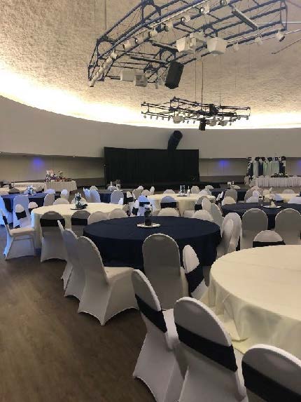 Banquet hall with round tables covered in white and dark blue tablecloths, arranged under modern lighting fixtures.