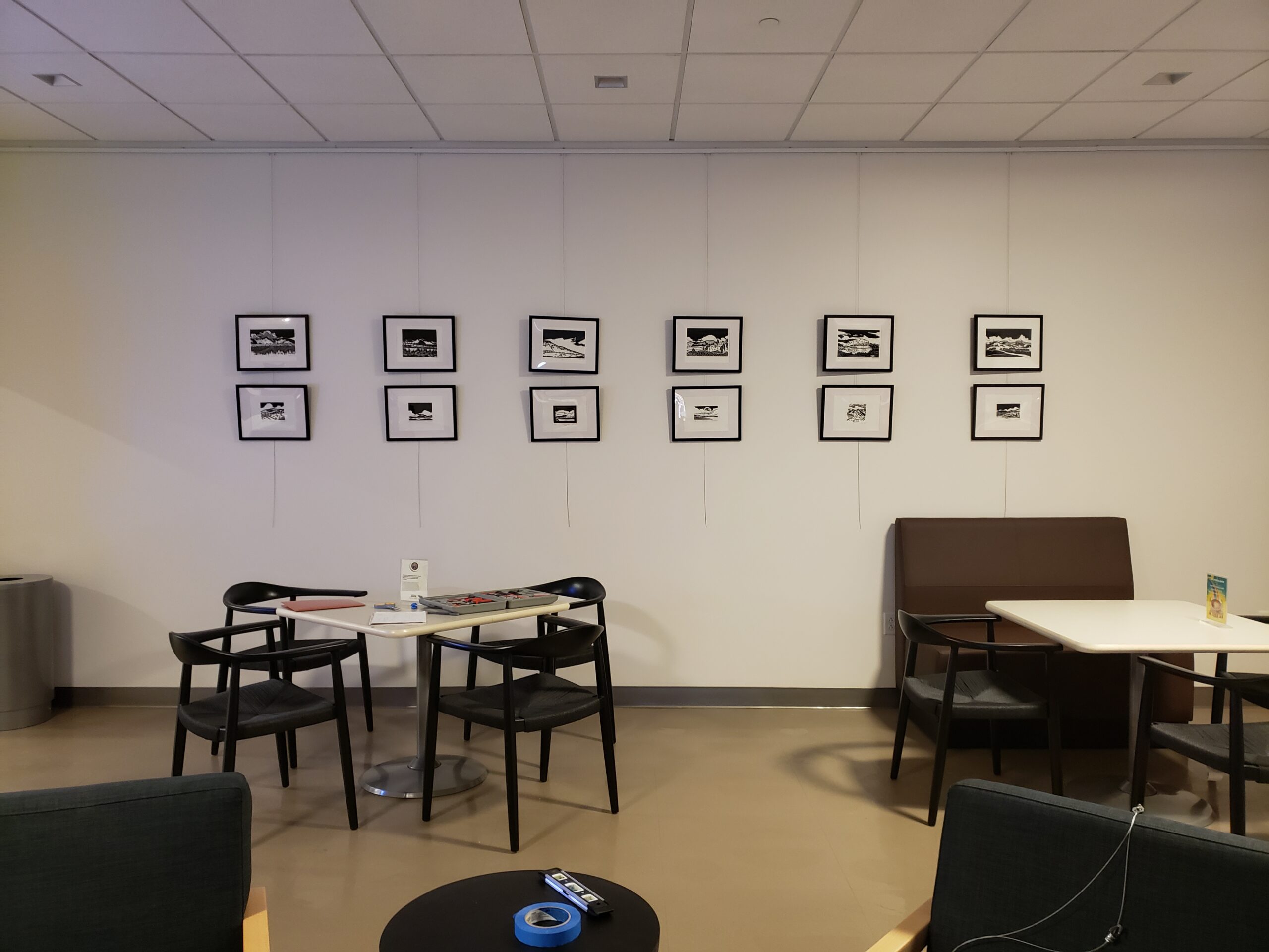 Wall with framed black-and-white photos above tables and chairs in a lounge area.