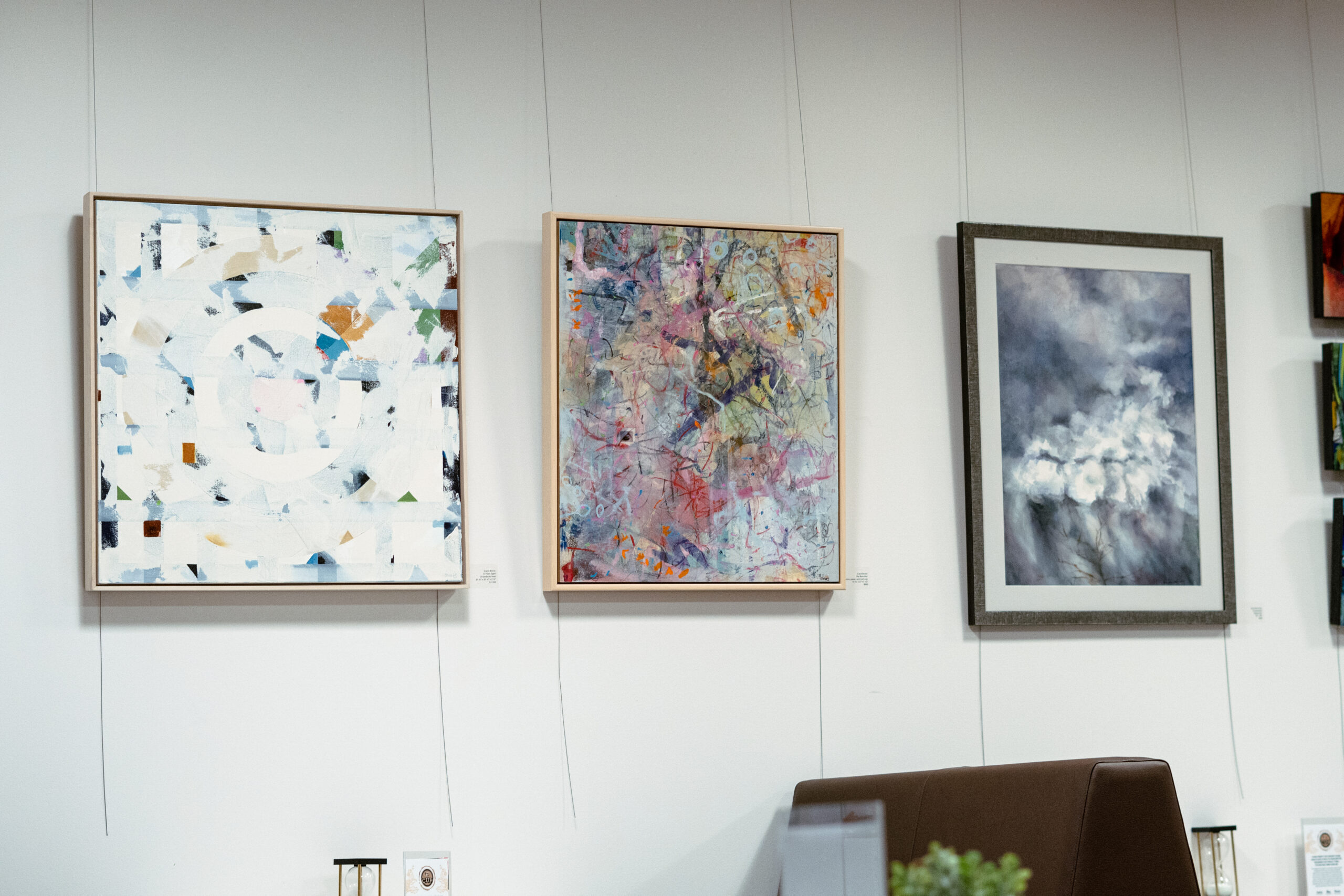 Three abstract paintings on a gallery wall, each with distinct textures