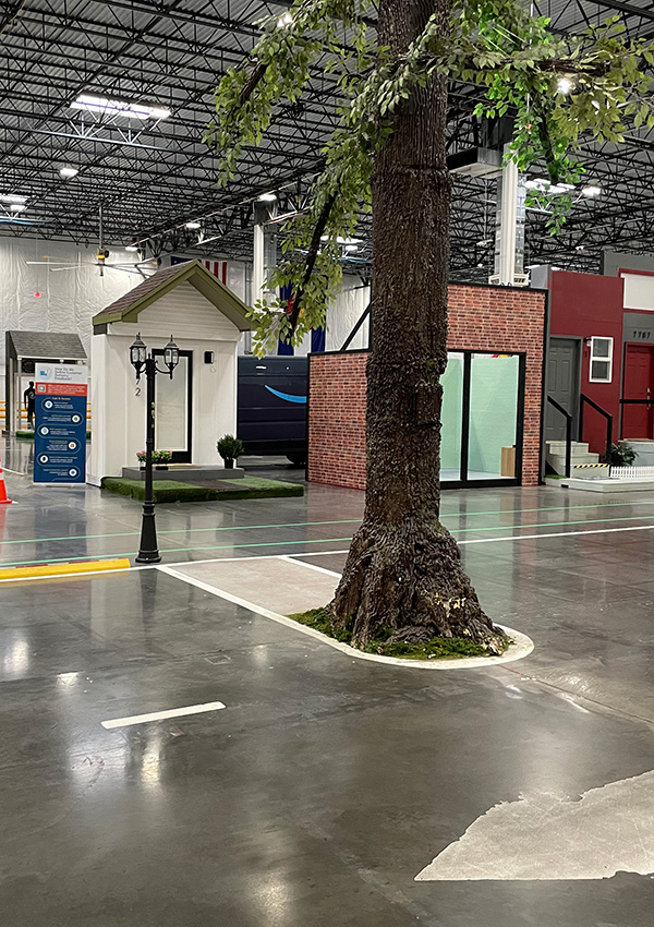 Indoor street simulation with a tree, lamppost, small house, and brick building.