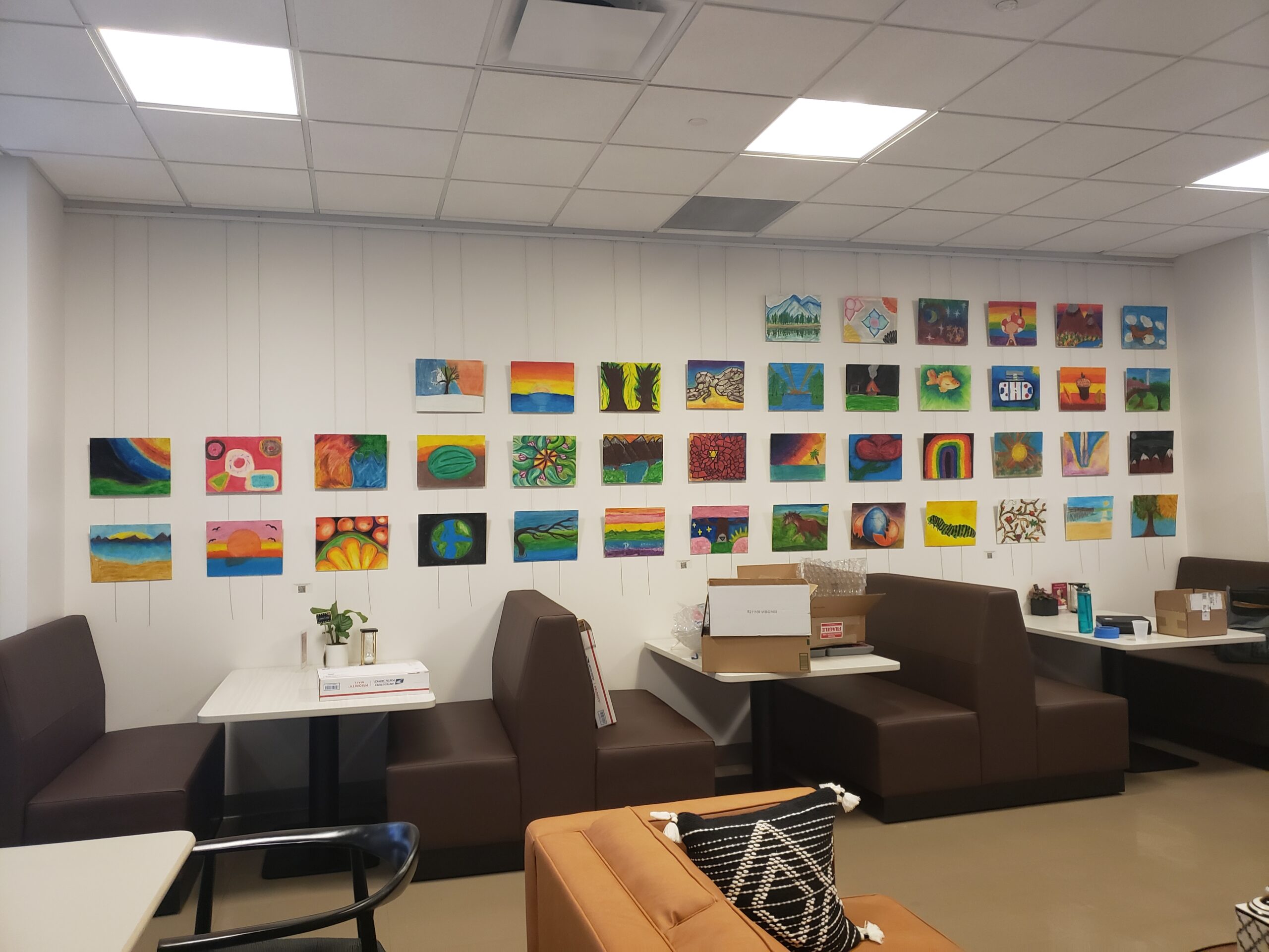 Booths and tables in a room with colorful artwork displayed on the wall above them