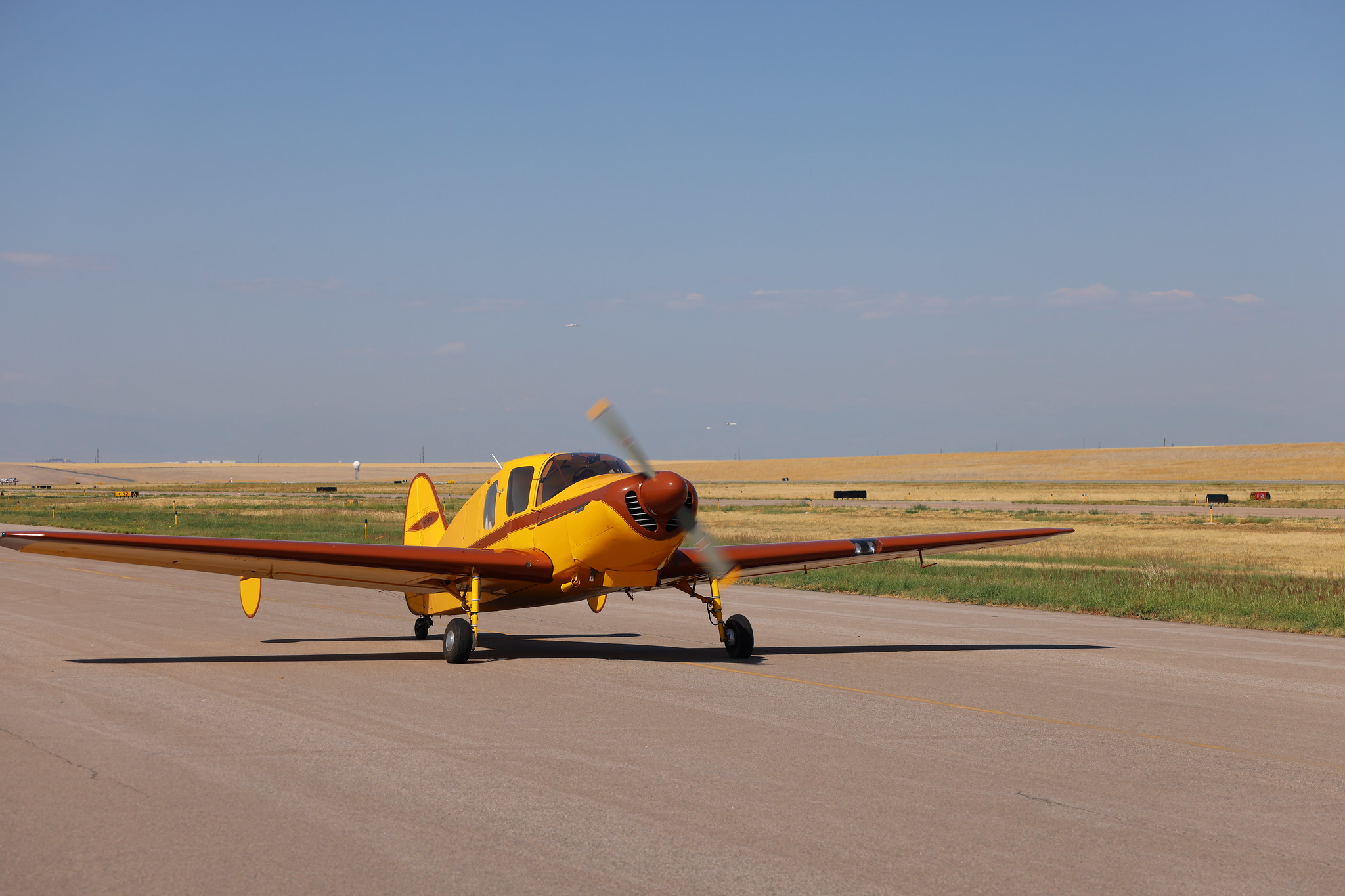Yellow and brown vintage airplane taxiing on a runway under clear blue sky.