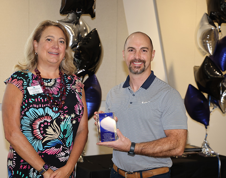 Two people at an event; one holds an award plaque with text.