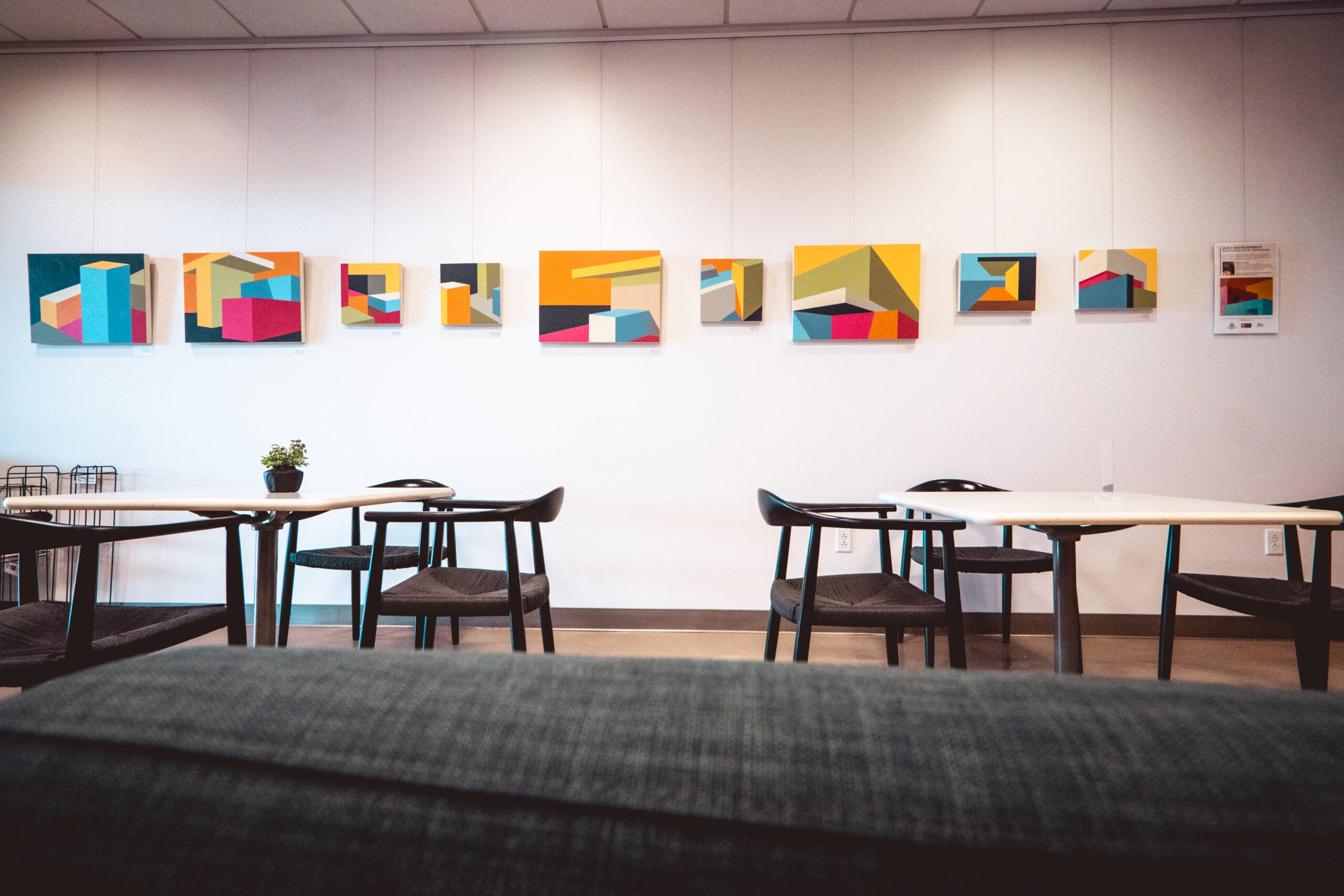 Colorful abstract art on a gallery wall above modern café seating.
