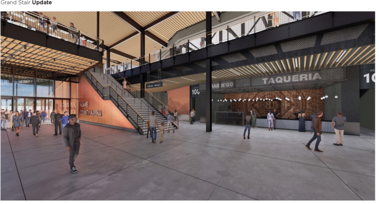 Grand stair in Adams County Arena; people walking, taqueria on right, overhead structure and railing above.