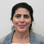 Carmen smiling with dark hair, denim jacket, neutral background