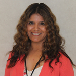 Christina Cruz smiling, wearing a coral cardigan and floral top