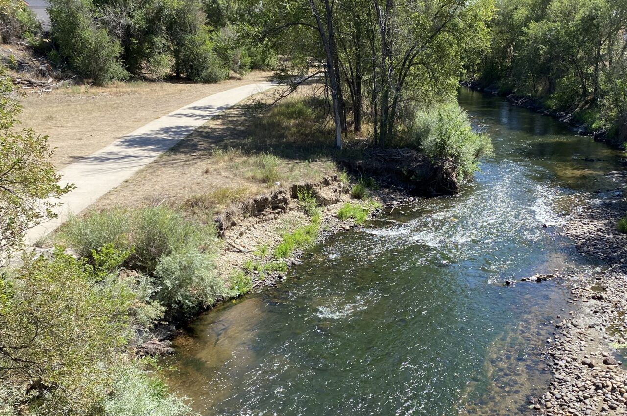 Clear Creek Trail with flowing river, trees, and rocky shoreline.
