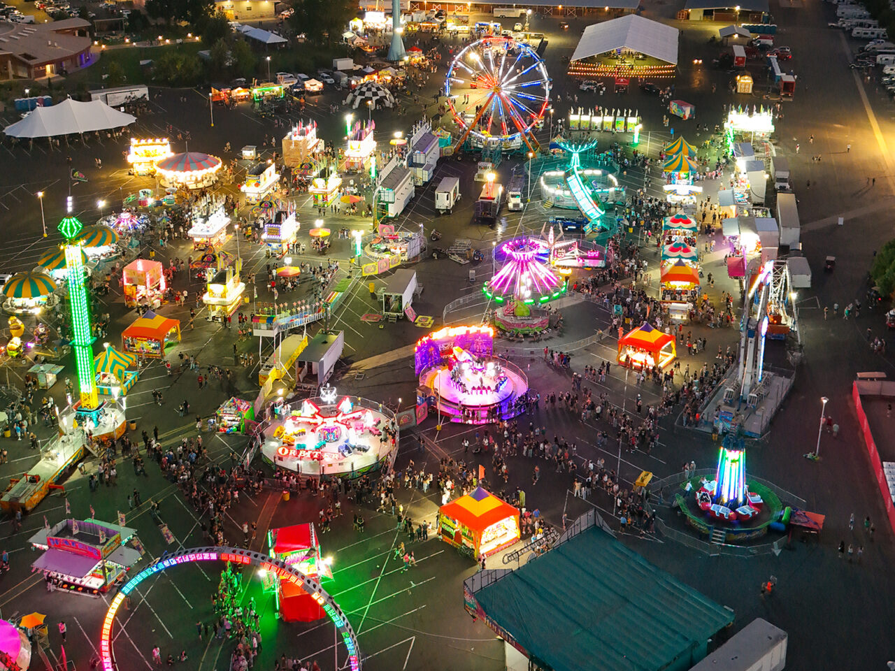 Aerial view of brightly lit Adams County Fair at night with various rides and colorful attractions.