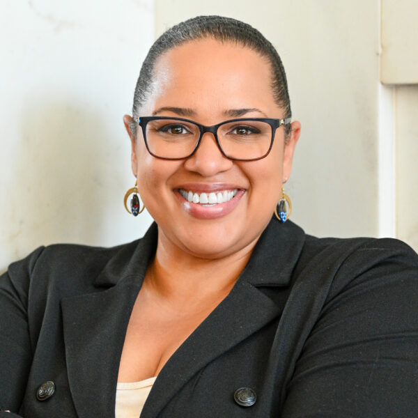 Dionne, smiling confidently, in a black blazer with arms crossed.