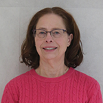 Elisa smiling, wearing glasses and a pink sweater, against a neutral background.