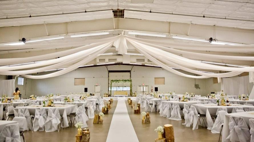 Wedding reception hall with draped ceiling, white-clothed tables, and a central aisle.