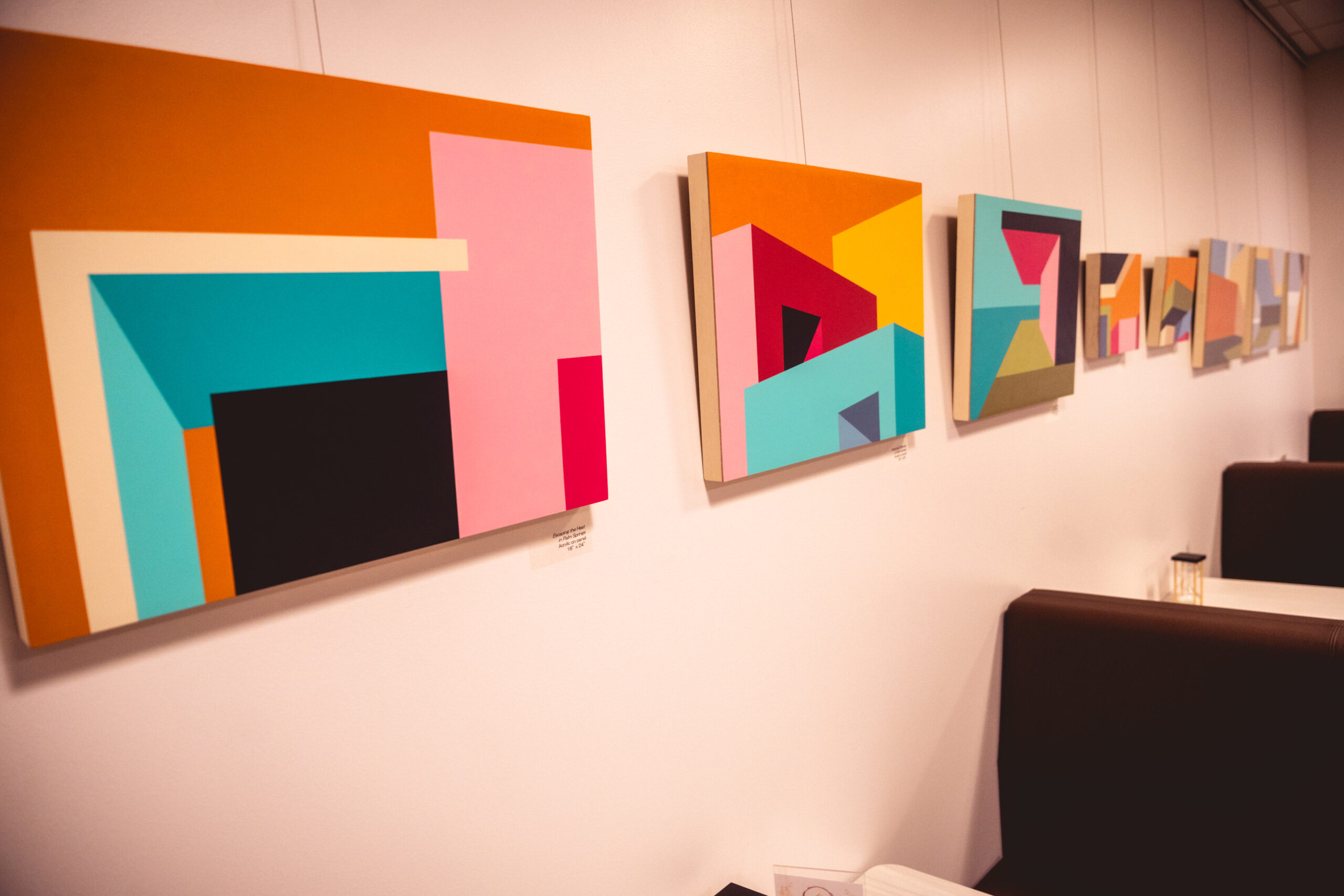 Abstract geometric paintings with vibrant colors hanging on a white wall in a gallery setting