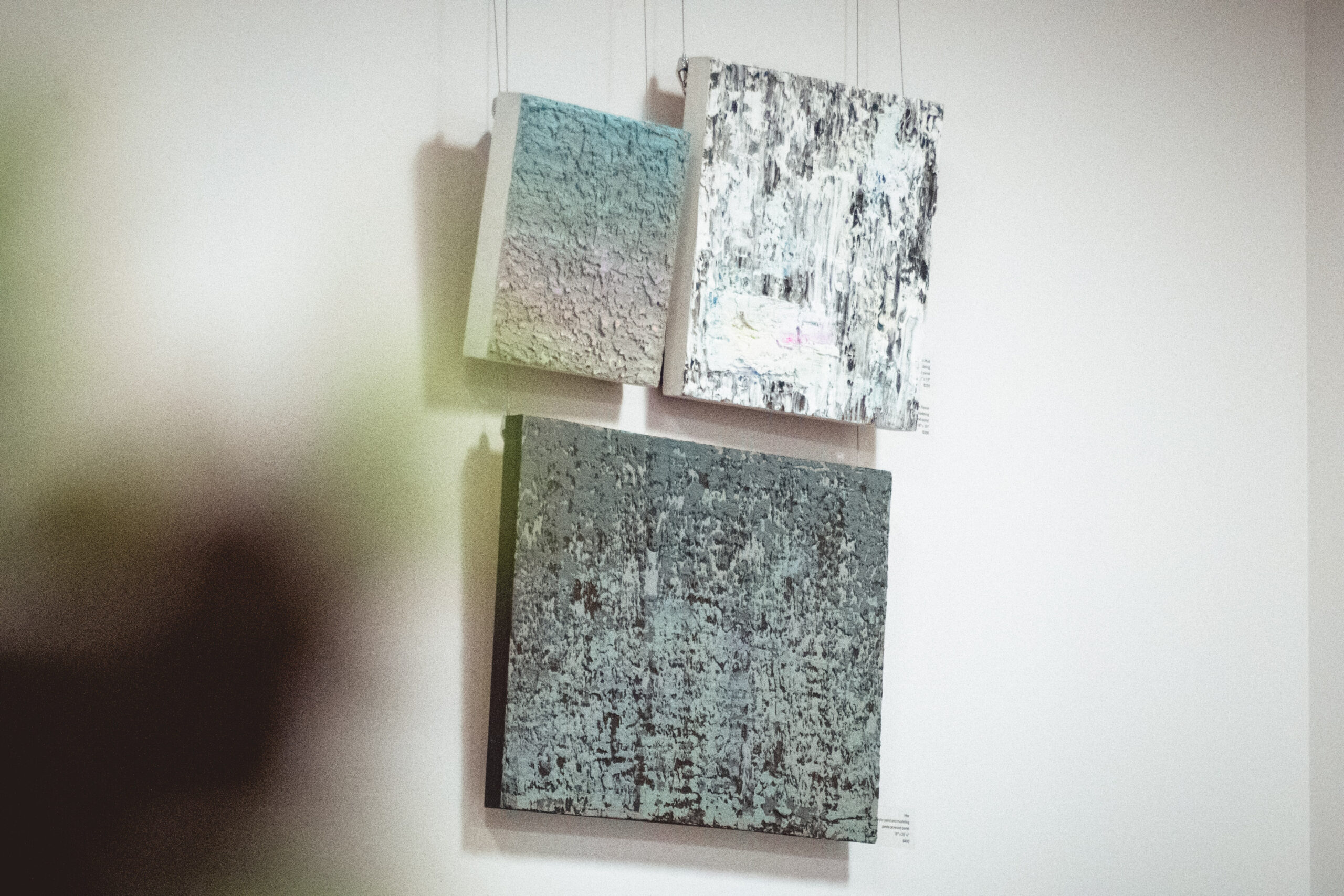 Three textured abstract paintings hanging on a light-colored wall