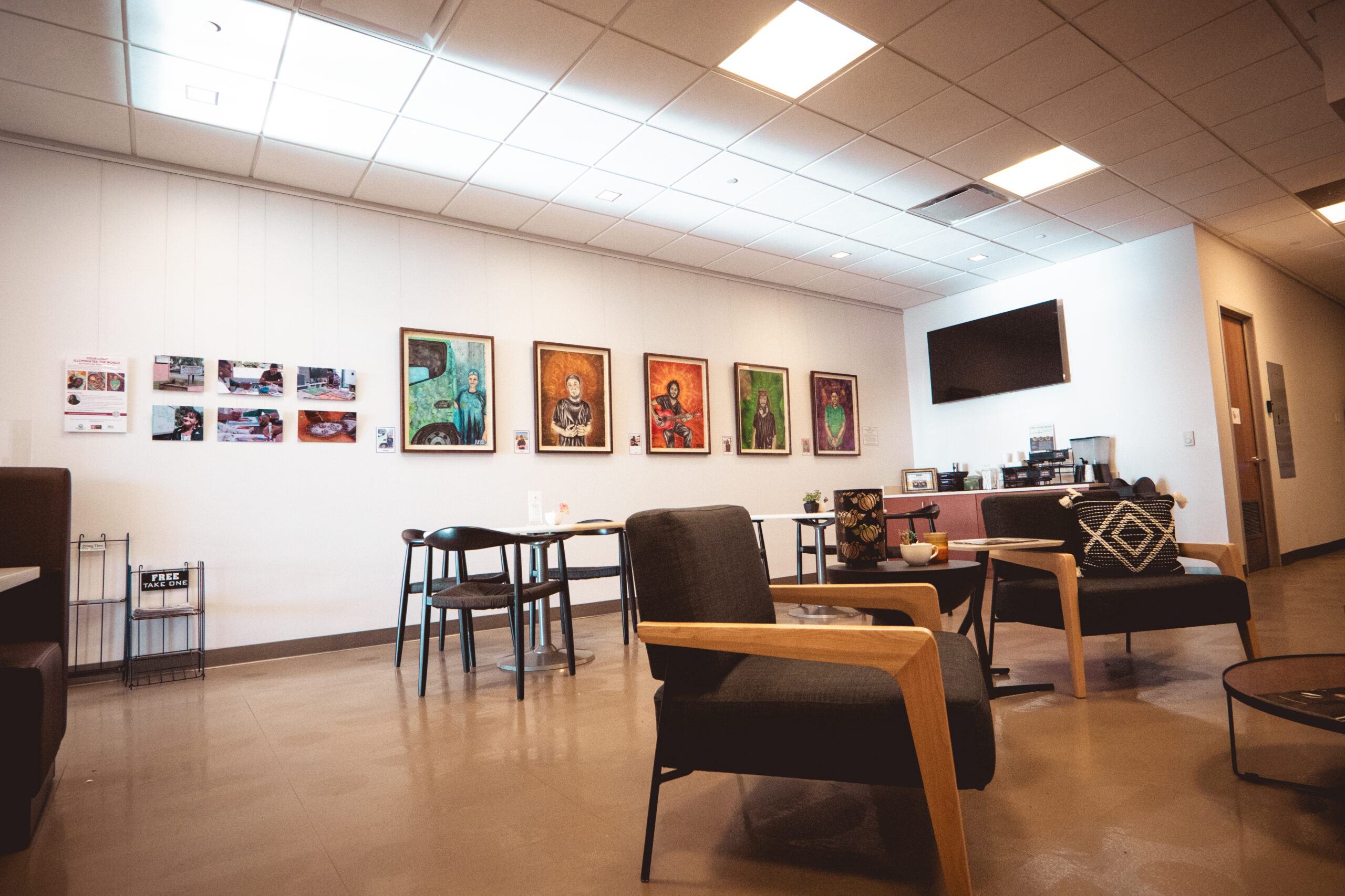 Art-filled waiting room with chairs, a table, and a TV mounted on the wall.