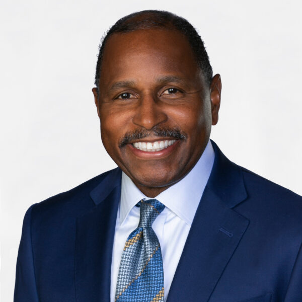 Faquir smiling in a blue suit and patterned tie against a neutral background