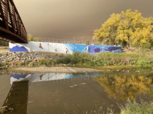Bridge over river, mural depicting wildlife, autumn trees reflecting in water.