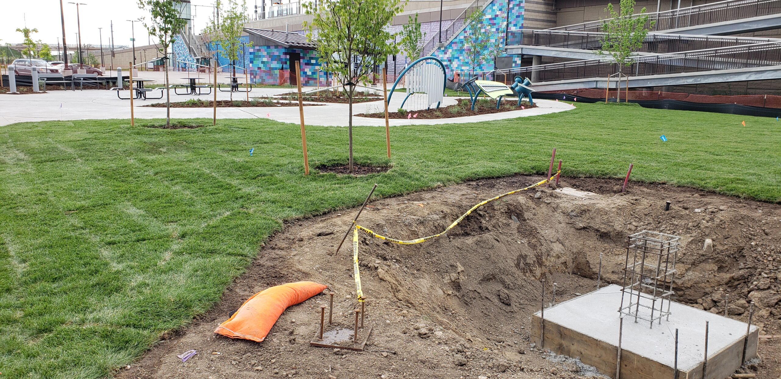 Construction site with fresh grass, trees, caution tape, and rebar in concrete base