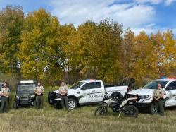 Group of park rangers standing by vehicles in a grassy field with autumn trees