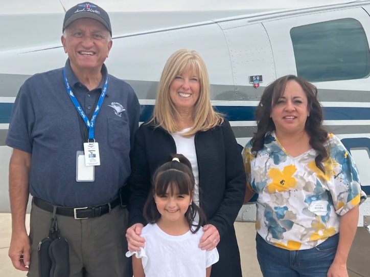 Four people smiling in front of a small airplane, one child included.