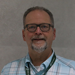 Jeff smiling in a plaid shirt, wearing glasses and a lanyard.