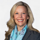 Jenni Hall smiling, wearing a blue scarf and gray blazer