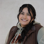 Karla smiling warmly in casual clothing, brown vest over hoodie