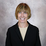 Leslie smiling in formal black blazer against a neutral background