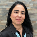 Monica Lujan smiling, wearing a black shirt, stone wall background