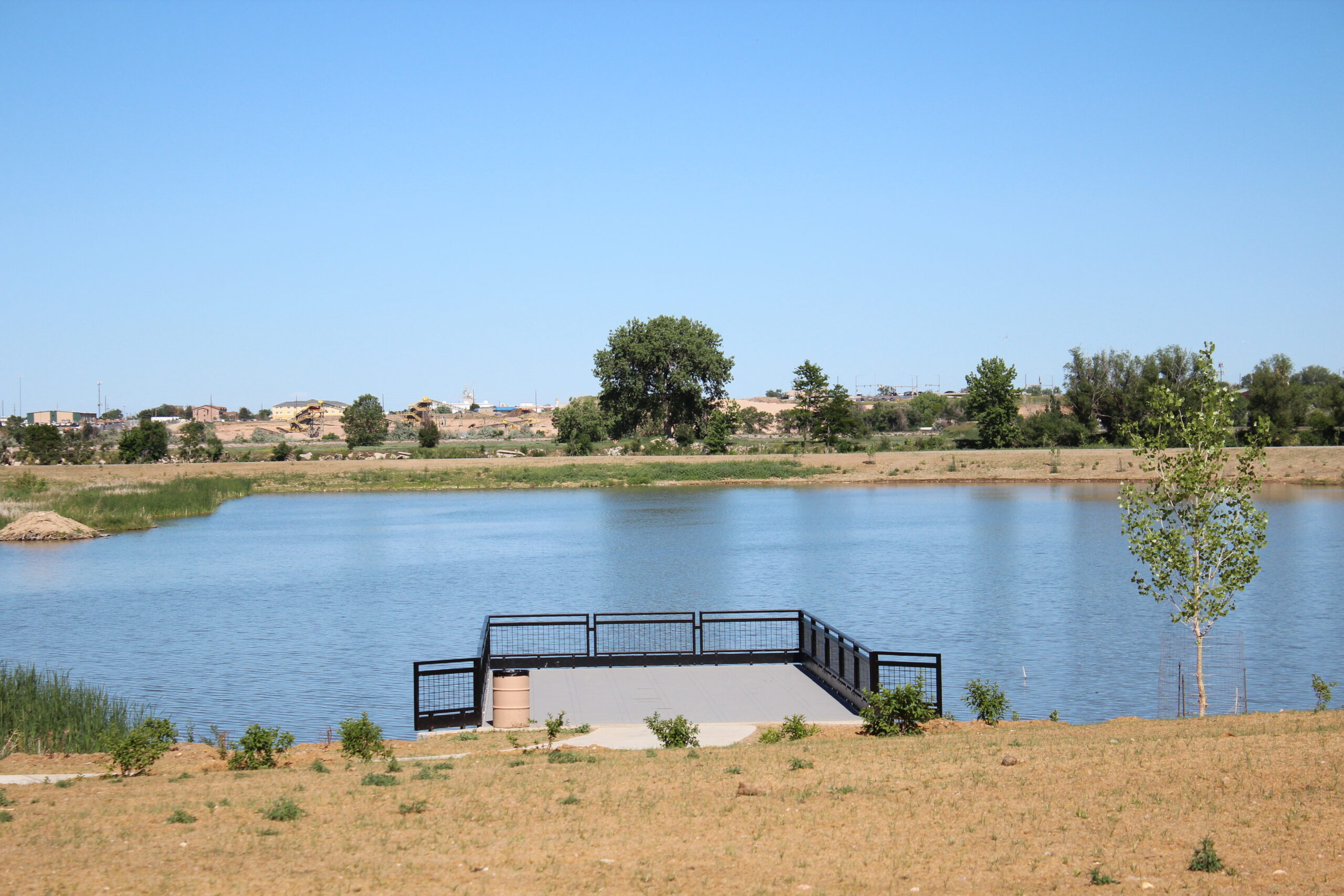 Deck overlooking a pond with a distant view of trees and buildings.
