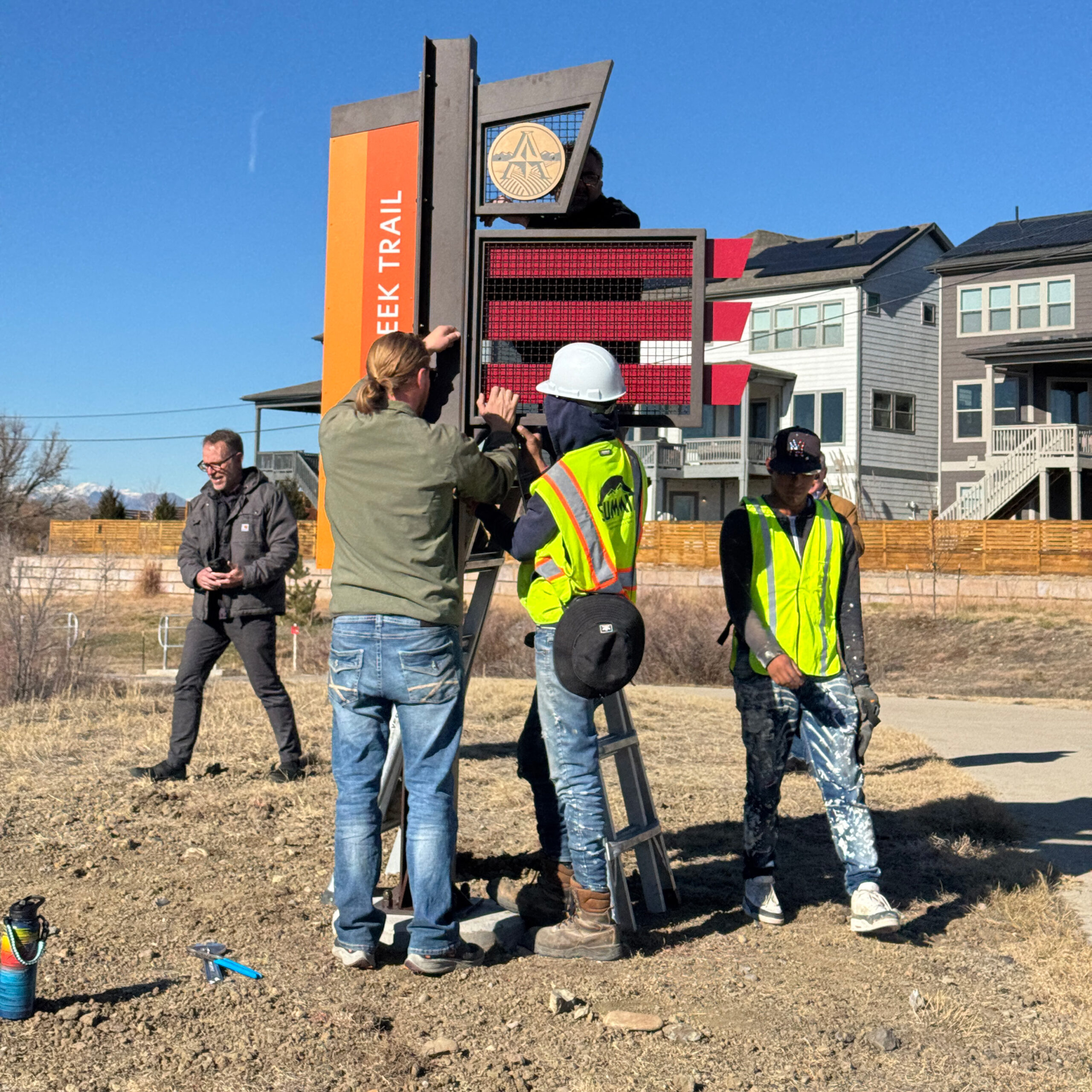 Workers installing sign for Oak Creek Trail in a sunny residential area