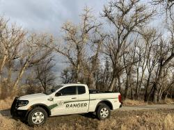 Ranger truck parked on dirt path, surrounded by leafless trees, under a cloudy sky.