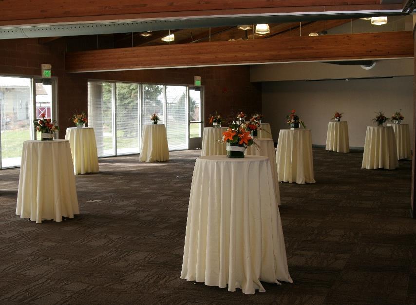 Spacious event room with round tables, white linens, floral centerpieces, and large windows.