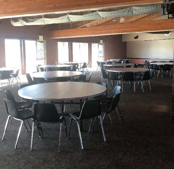 Spacious room with round tables, black chairs, and bright windows.