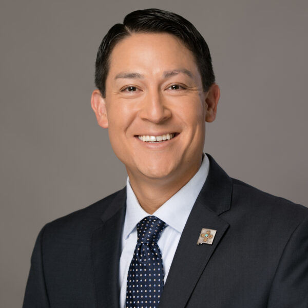 Rivera_headshot.jpg man smiling in a suit with a pin badge