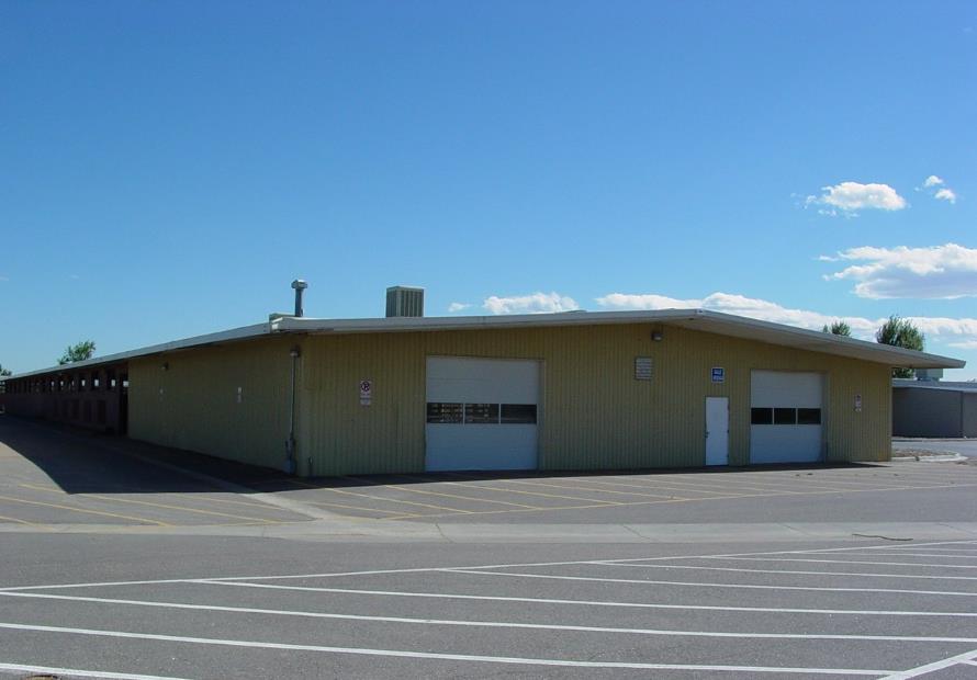 Yellow warehouse building under clear blue sky, featuring garage doors and a "No Parking" sign.