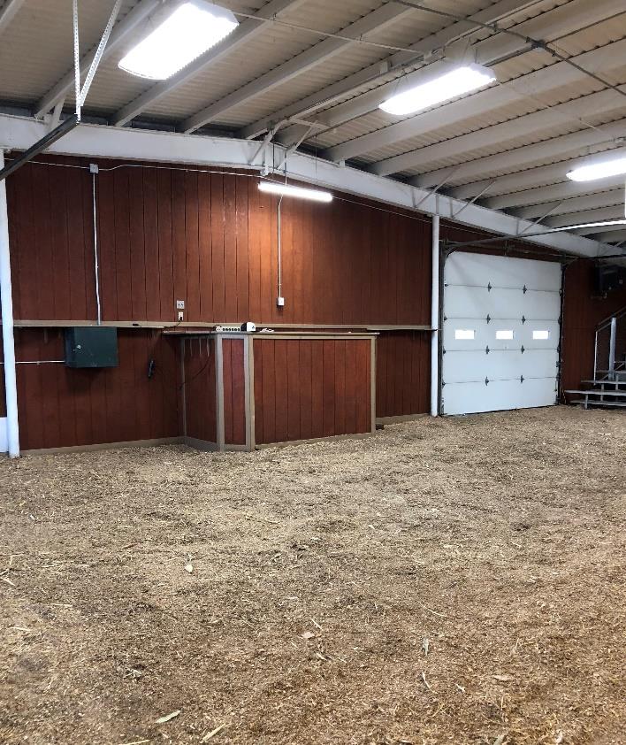 Well-lit barn interior with a red wooden wall, overhead lights, and a closed garage-style door.