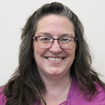Sandra smiling with long hair and glasses, wearing a purple shirt.