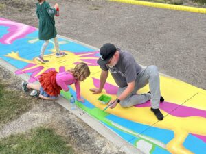 Man and child painting colorful sidewalk mural outdoors