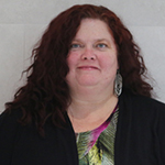 Shannon smiling warmly, with long curly brown hair, wearing a black blazer.