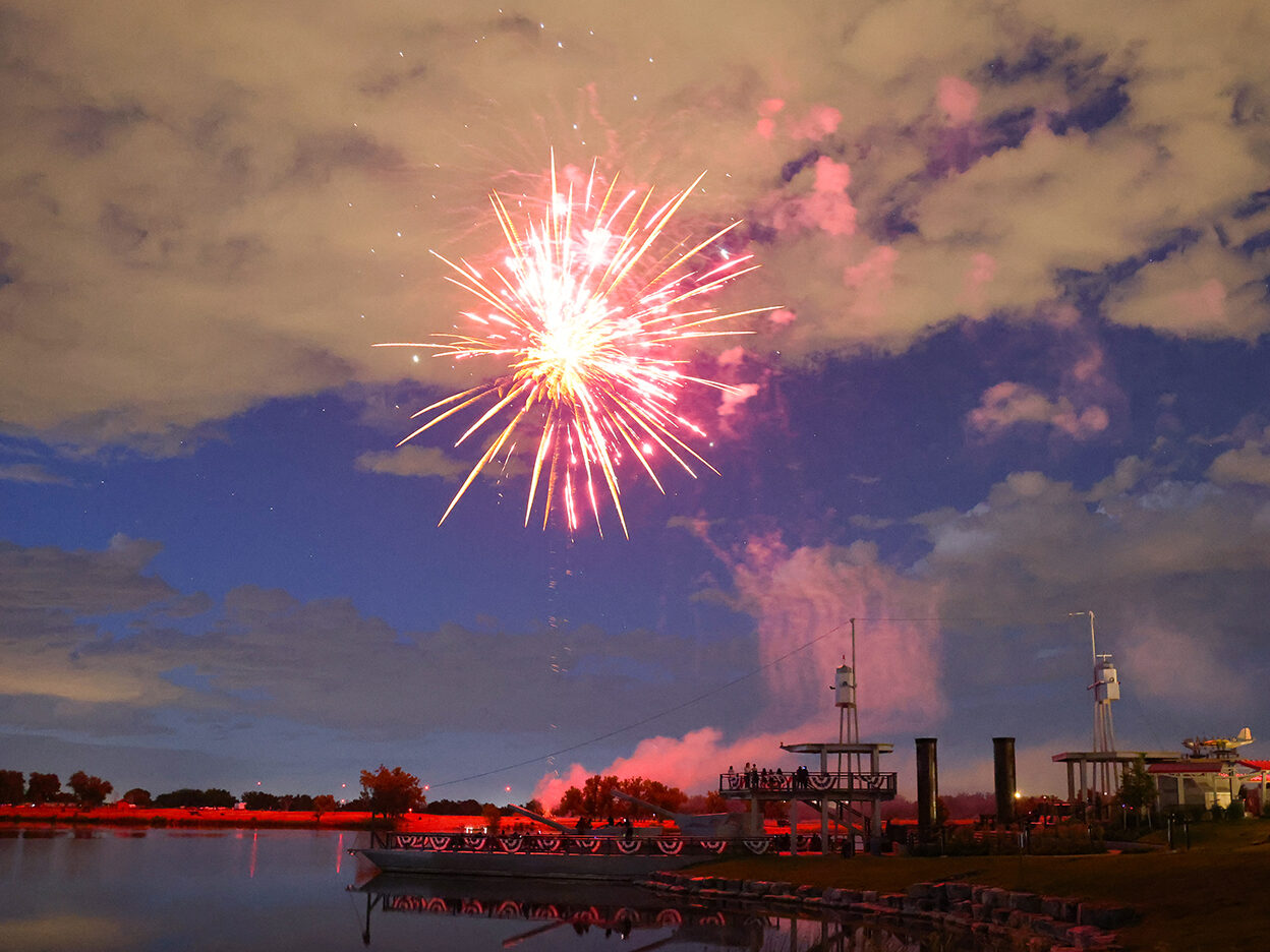 Fireworks explode in the night sky over a lake with reflections.