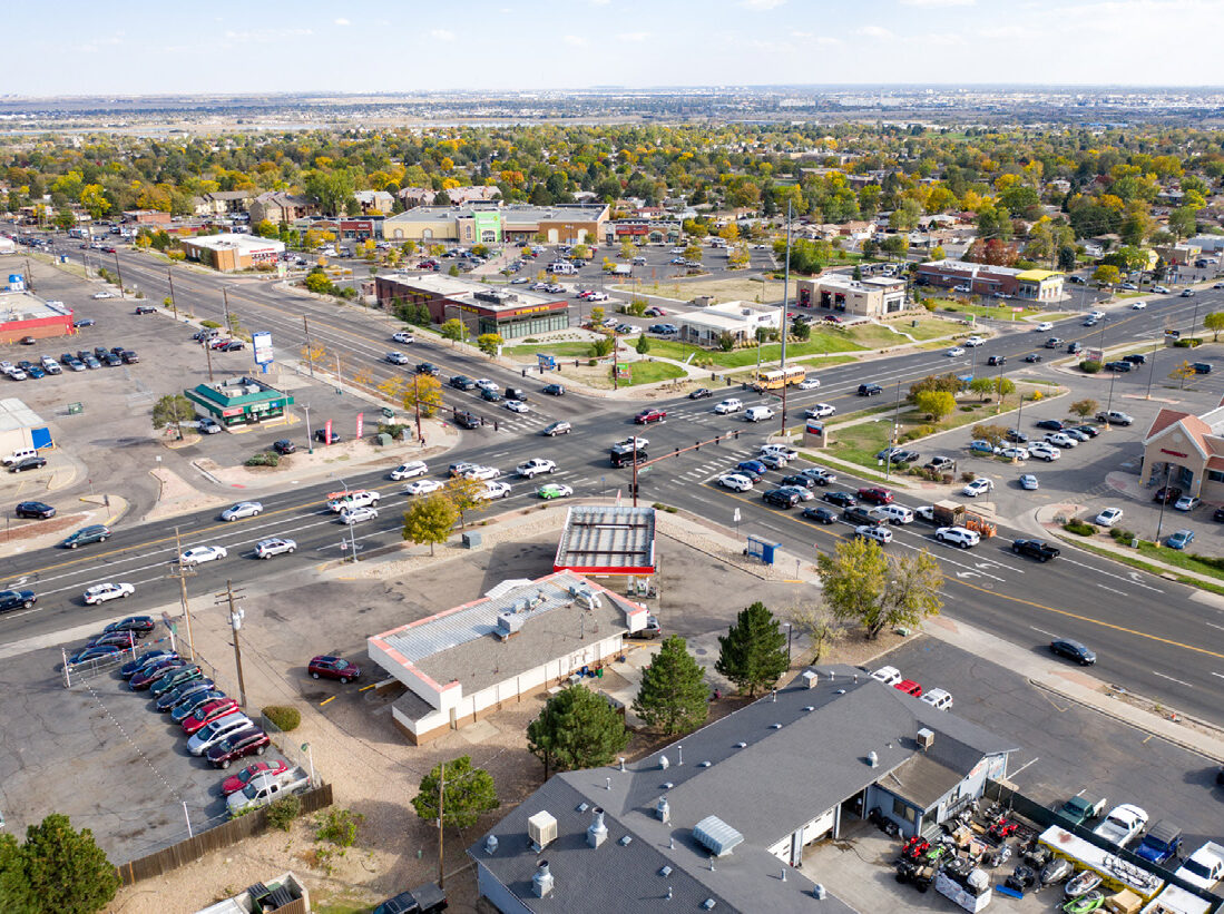 Aerial view of a busy intersection with surrounding businesses, including a Walgreens, and numerous cars parked and driving.