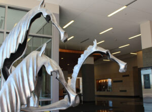 Three silver horse head sculptures in a modern building hallway