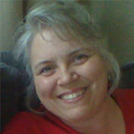 Vickie smiling warmly, wearing a red top, with gray hair.