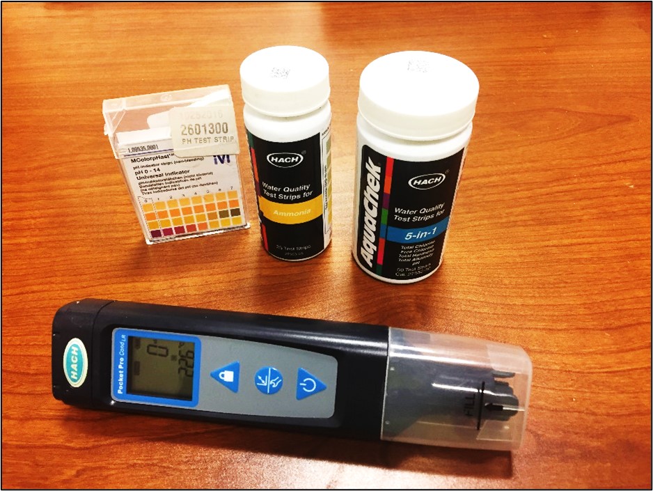 Water-Testing equipment on a table, including HACH test strips for ammonia and 5-in-1, pH color chart.