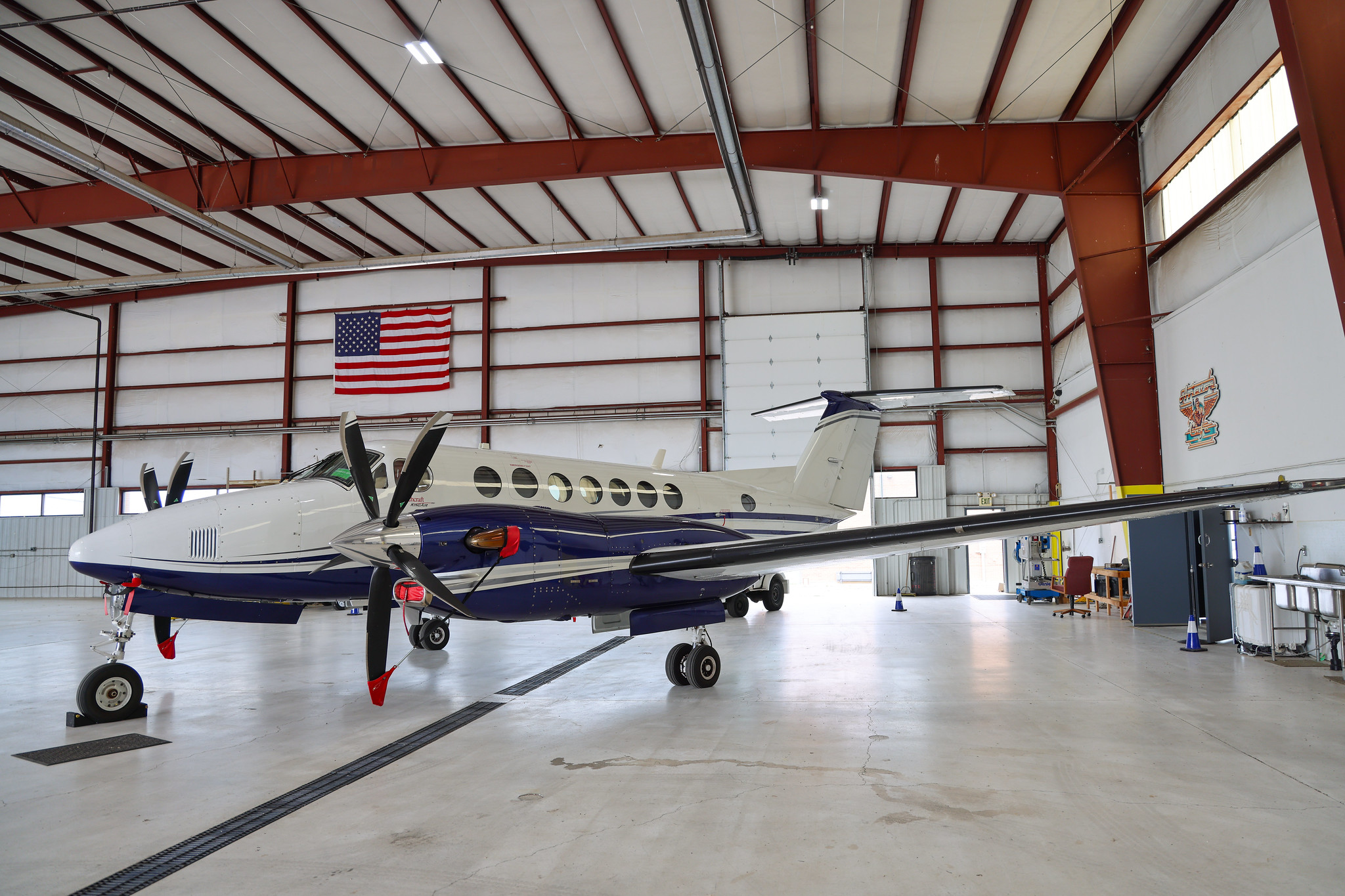 Aircraft in a large hangar with an American flag displayed.