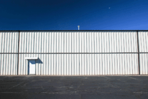 Metal warehouse exterior with a single small door under a clear blue sky.