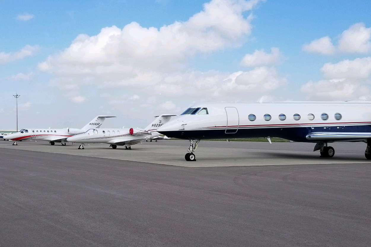 Three private jets parked on an airport tarmac under a blue sky.