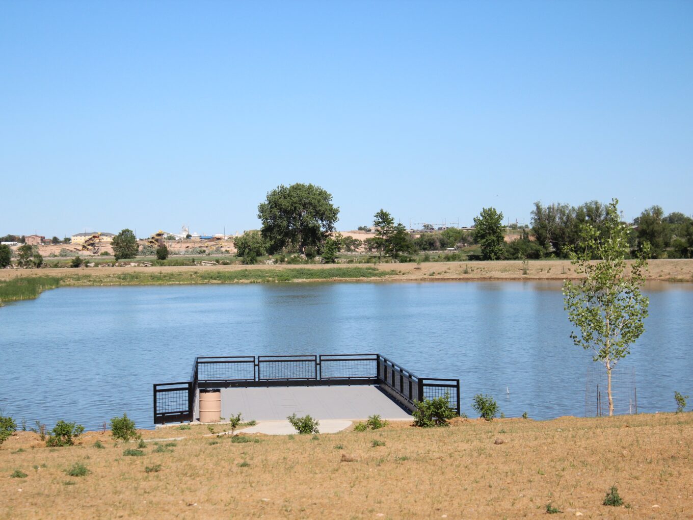 Wooden platform overlooking a calm lake, distant trees, and clear sky